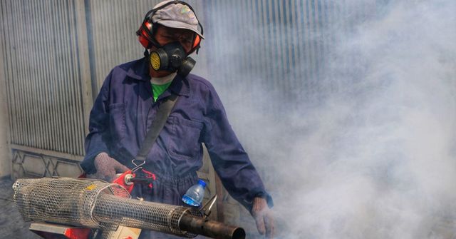 Man in protective gear fumigating with a fog machine outside.