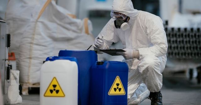 Person in hazmat suit inspecting barrels with radiation symbol. Industrial setting.