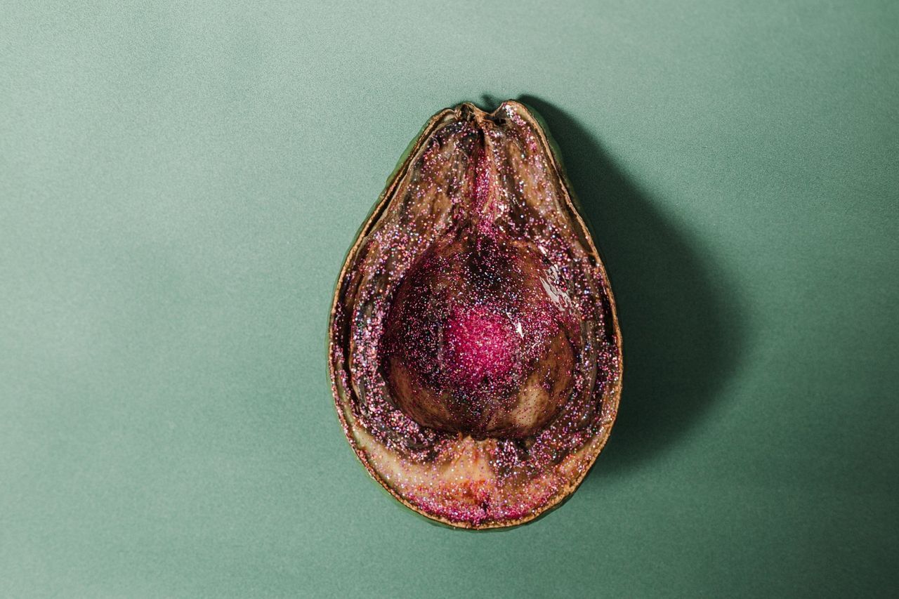 Cross-section of an avocado, brown with a dark center and red seed pocket, on a green surface.