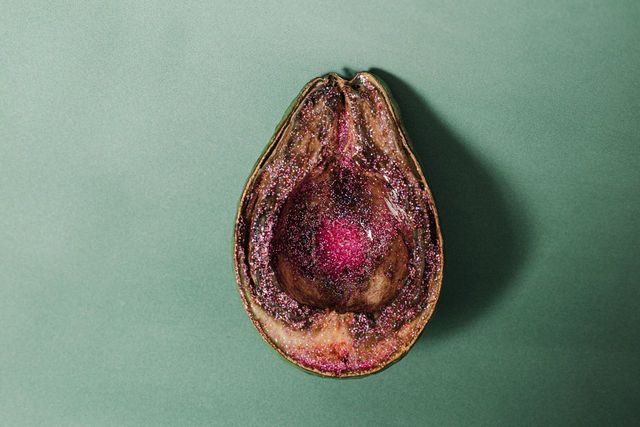 Cross-section of an avocado, brown with a dark center and red seed pocket, on a green surface.