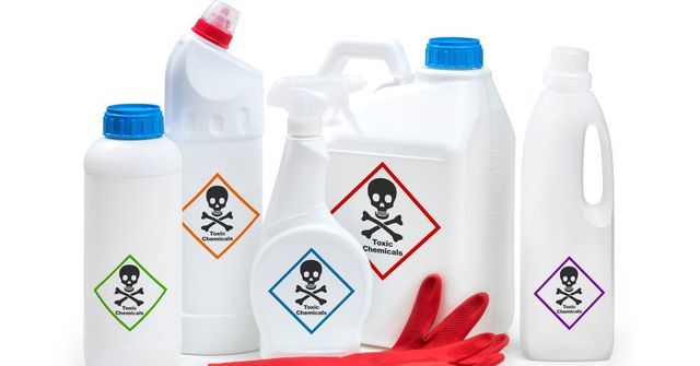 Assortment of white cleaning product containers with skull and crossbones hazard labels; red gloves.